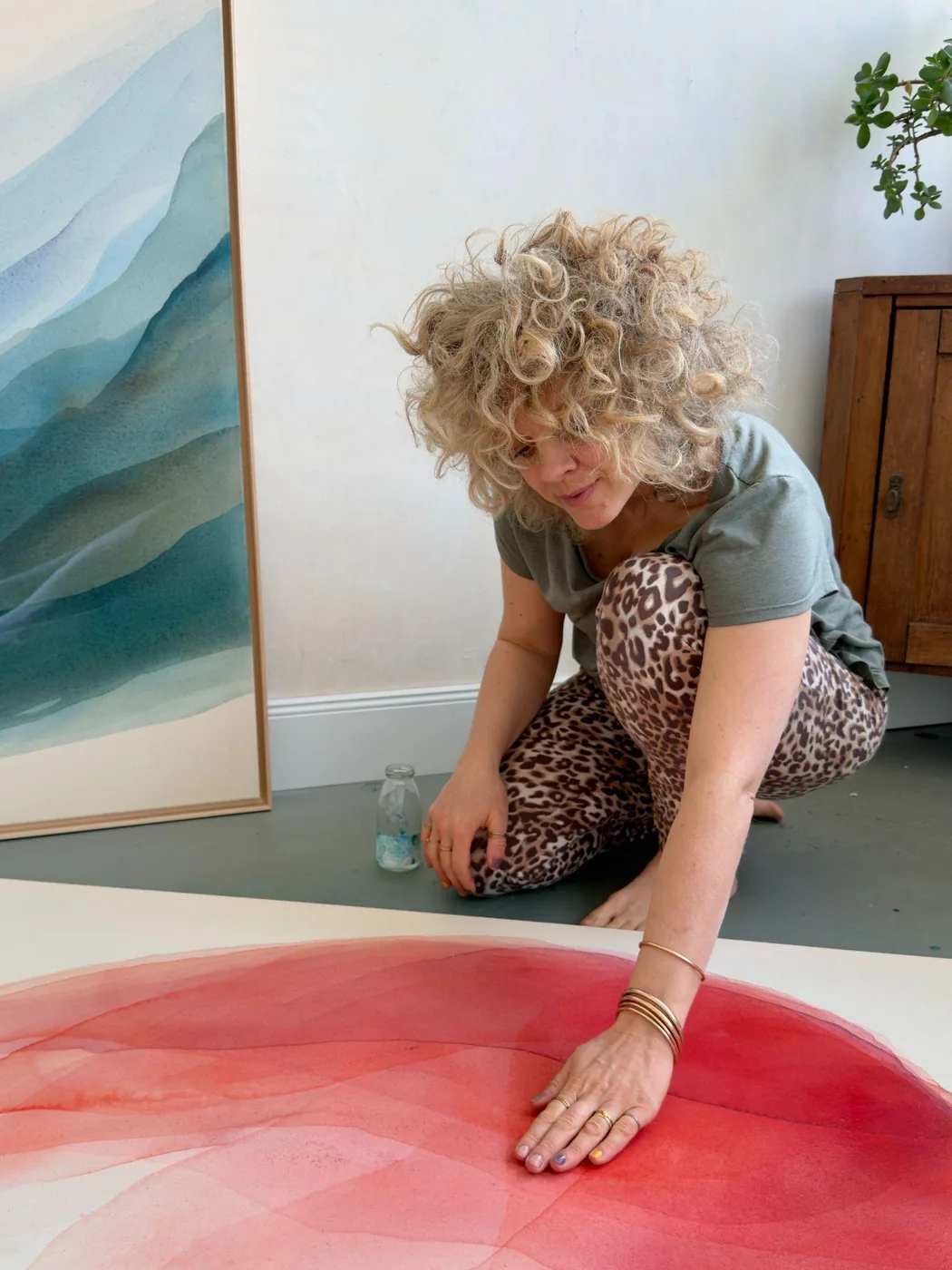 Johanne Bossmann malt mit der Hand auf einer Leinwand in Rottönen, daneben ein gerahmtes Werk in Blau
