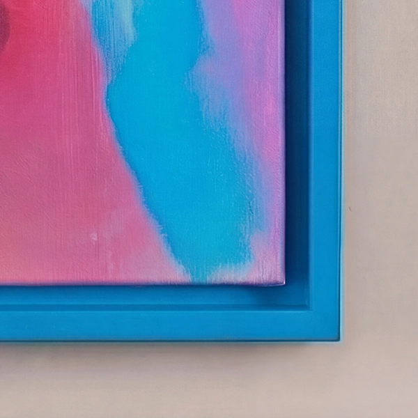 Nahaufnahme eines blauen Schattenfugenrahmens mit bunter Leinwand in Pink und Türkis vor einer hellbeige-farbenen Wand.